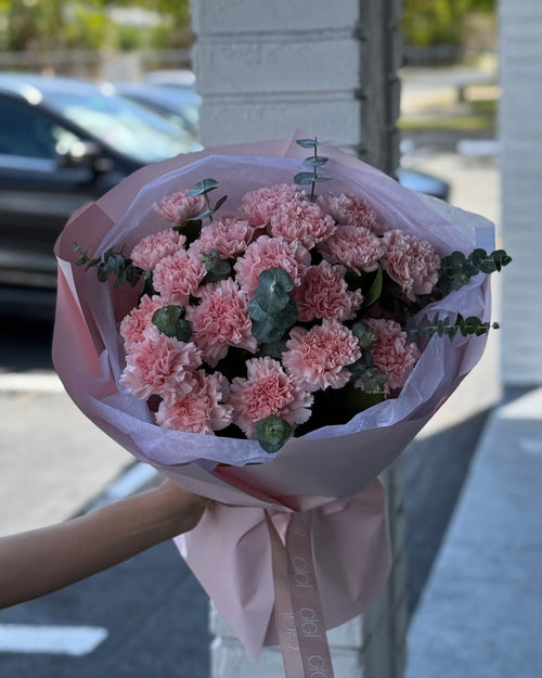 A bouquet of pink carnations wrapped in paper with a visible brand name on the tape.