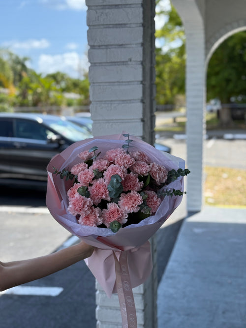 A bouquet of pink carnations wrapped in paper with a visible brand name on the tape.
