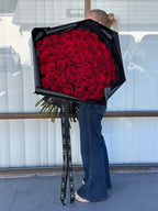 Person holding a large bouquet of red roses wrapped in black paper.