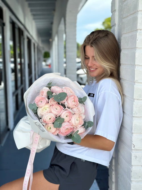 Woman holding a bouquet of pink flowers leaning against a wall.