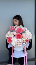 Person holding a large bouquet of pink and white flowers against a neutral background