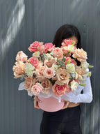 A person holding a round pink box with a bouquet of roses in various shades of pink, white, and beige.