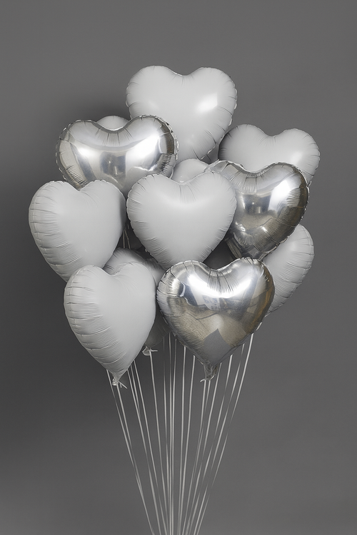 Bunch of heart-shaped balloons in silver and white on a dark background