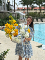 Woman holding a bouquet of yellow and white flowers by a poolside.