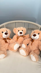 Four teddy bears with brown bows sitting on a white surface against a light blue wall.
