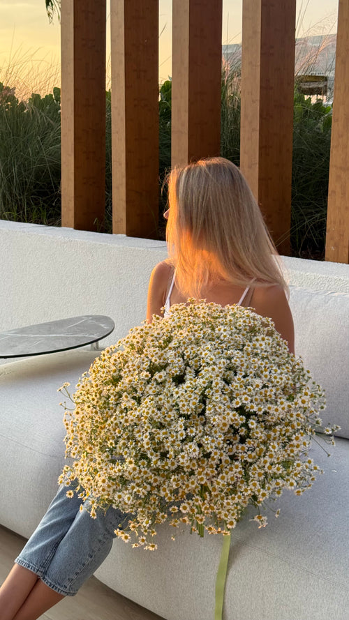 Woman holding a large bouquet of flowers sitting on a couch outdoors.
