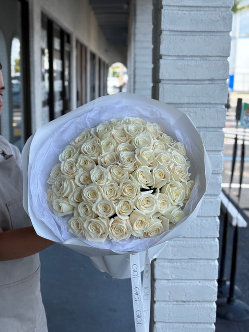 A bouquet of white roses being held by a person, wrapped in white paper.