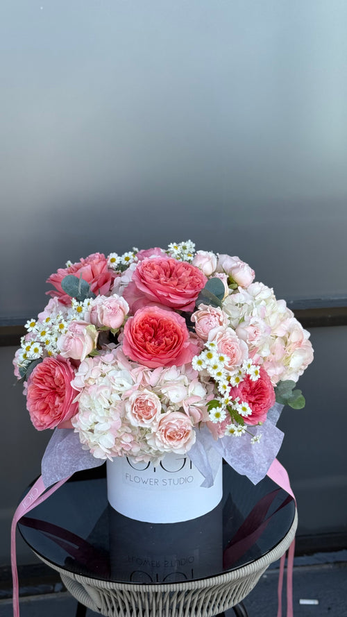 Bouquet of pink and white flowers in a box on a reflective surface with a neutral background
