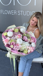 Woman holding a large bouquet of flowers in front of a 'Flower Studio' sign.
