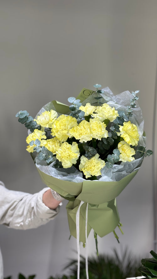 A bouquet of pink carnations wrapped in paper with a visible brand name on the tape.