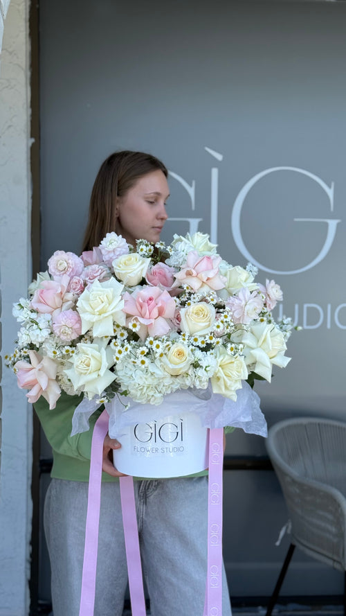 Person holding a large bouquet of flowers in front of a store with 'Gigi' branding.