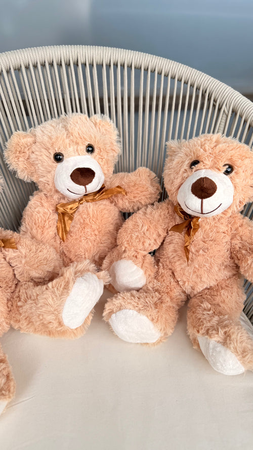 Two teddy bears sitting on a white chair against a light blue wall.