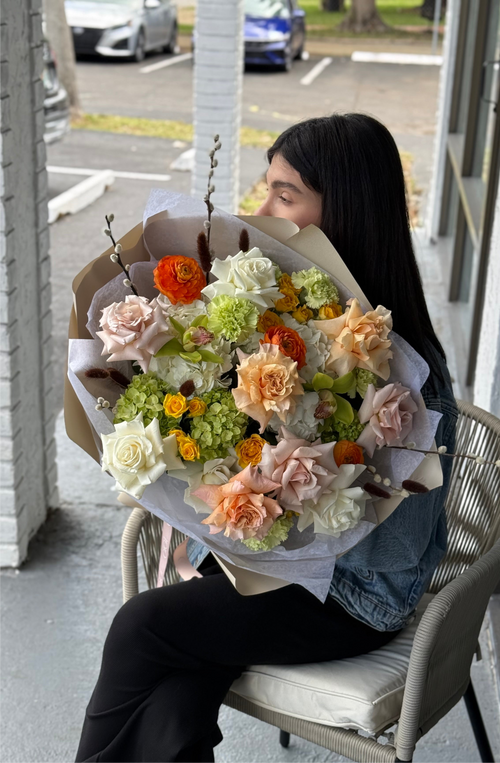 A person sitting on a chair holding a bouquet of flowers with a variety of colors including white, green, orange, and pink.
