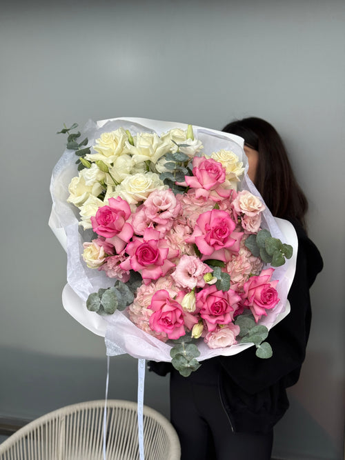 Person holding a large bouquet of pink and white flowers against a plain background