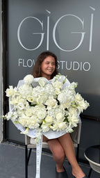 Woman holding a large bouquet of white flowers in front of a 'Gigi Flower Studio' door.