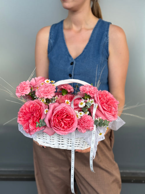 Person holding a white basket filled with pink flowers against a neutral background