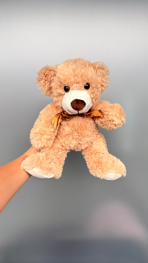 Beige teddy bear held by a hand against a gray background