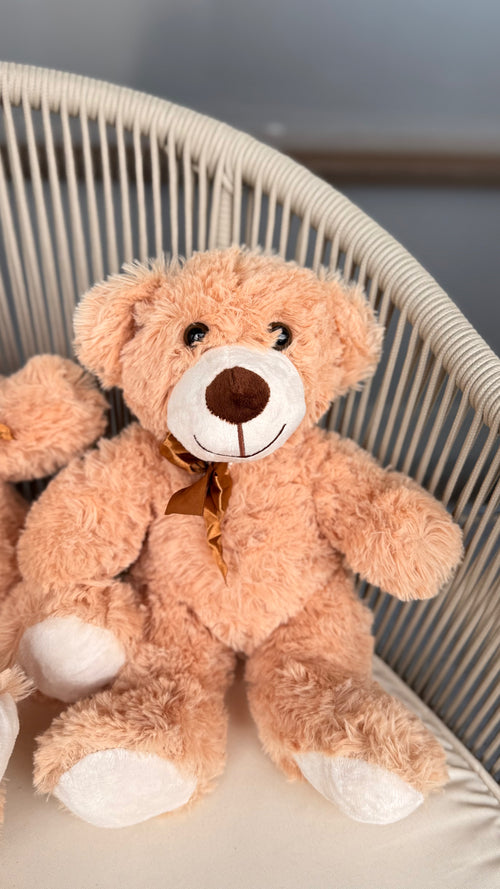 Plush teddy bear with a bow tie sitting in a wicker basket.