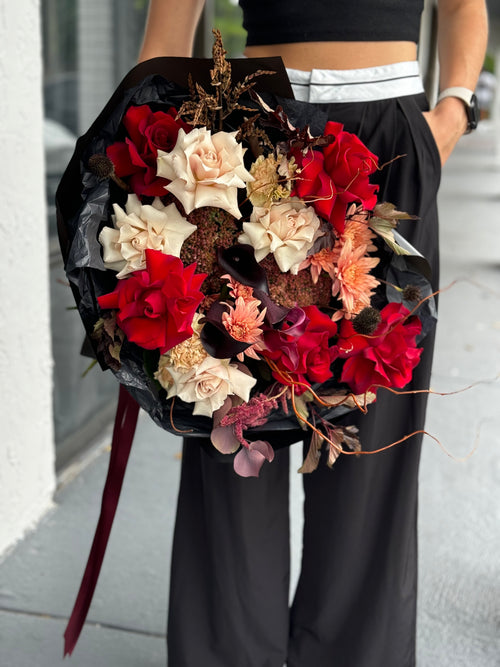 Person holding a bouquet of red, white, and orange flowers with black accents.