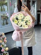 A person holding a bouquet of white ranunculus flowers wrapped in pink and white paper with a ribbon.