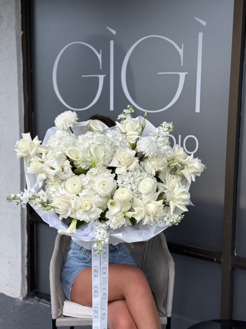 Bouquet of white flowers held by a person in front of a store with 'GIGI' branding.