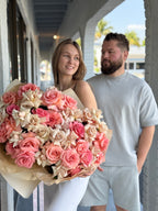 A person holding a large bouquet of flowers with a mix of pink, white, and red colors, standing next to a man who is smiling.