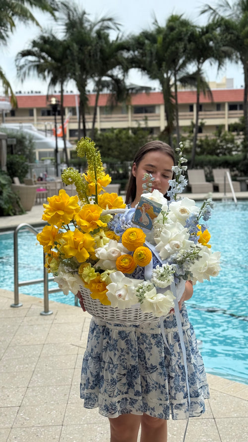 Woman holding a large basket of flowers by a poolside with palm trees in the background