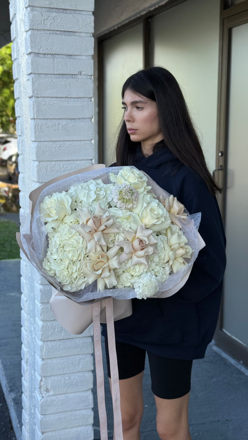 Woman holding a large bouquet of white flowers against a building.