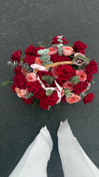 Heart-shaped arrangement of red and pink roses with greenery on a dark surface.
