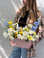 A person holding a pink floral handbag with a variety of flowers including white, yellow, and blue blooms.