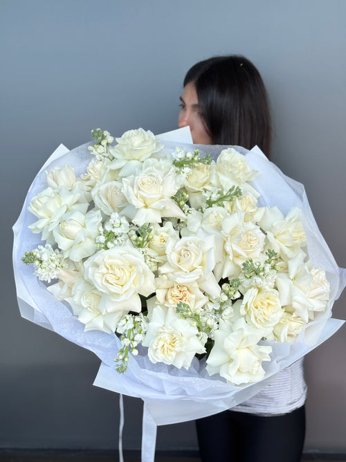 Person holding a large bouquet of white flowers against a gray background
