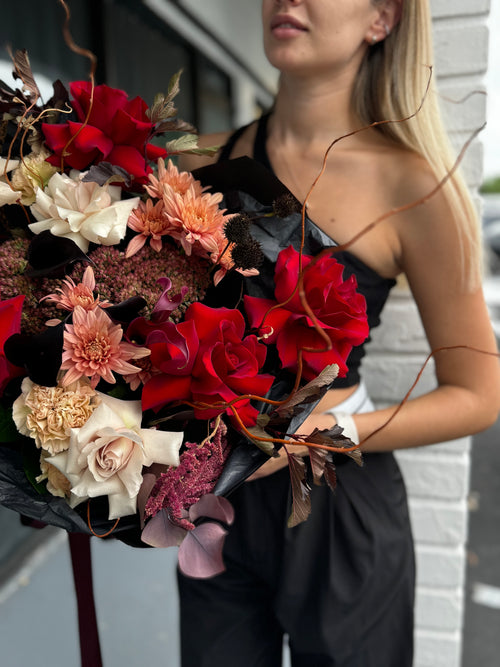 Woman holding a bouquet of red, white, and pink flowers against a blurred background