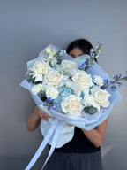 Person holding a bouquet of white and blue flowers against a gray background