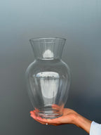Clear glass vase held in a hand against a gray background