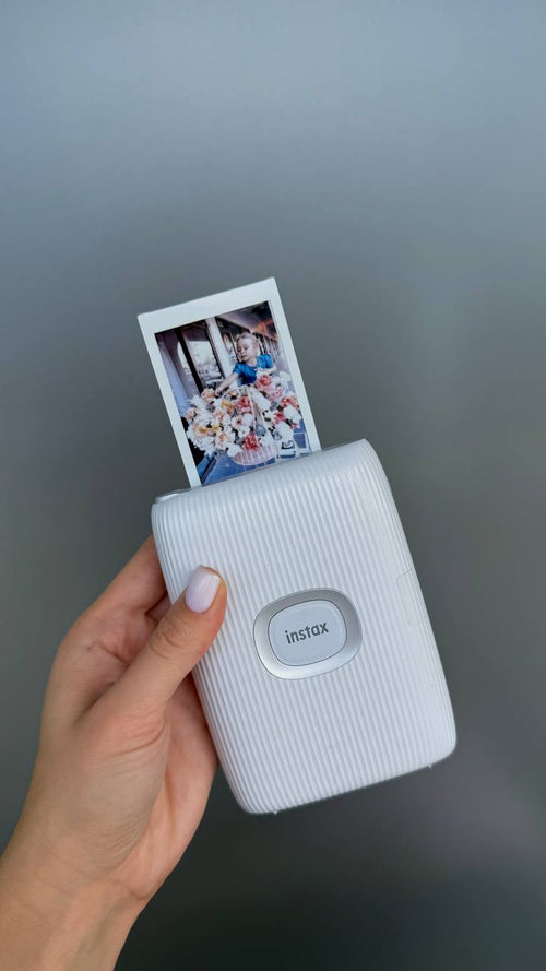 Instax printer with a photo attached, held against a gray background