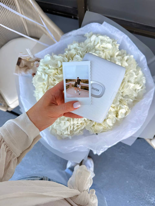 Person holding a Polaroid photo in front of a bouquet of white flowers