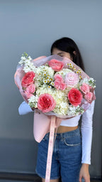 Person holding a bouquet of pink and white flowers against a plain background