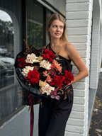 A person holding a bouquet of flowers with a mix of red, black, and white colors.