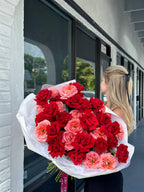 A person holding a large bouquet of red and pink flowers.