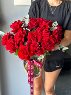 A person holding a vase with French twisted red roses and green leaves.