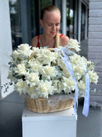 A woman sitting behind a luxurious floral arrangement consisting of 50 white French roses in an elegant basket.