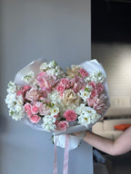 A bouquet of flowers including roses in white, pink, and red colors, wrapped with white paper and pink ribbon.