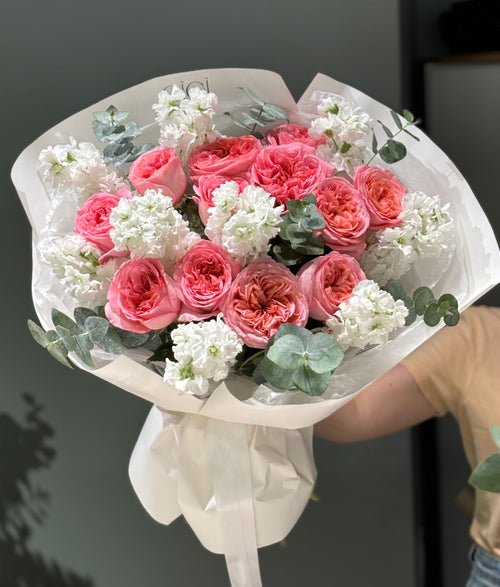 A bouquet of pink roses, white lilies, and other flowers, wrapped in white paper and ribbon.