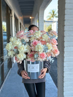A person holding a box of arranged roses with a mix of white and pink colors.