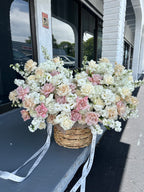 A floral basket arrangement with a variety of flowers including white and pink blooms, placed outdoors.
