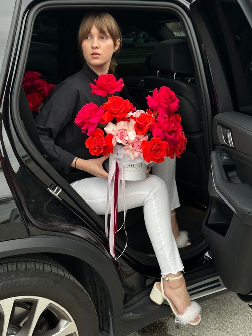 A person holding a bouquet of mixed pink and red roses climbing out of a car.