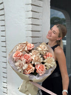 A person holding a large bouquet of flowers with a range of warm colors, predominantly pink and beige.