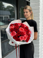 A person holding a bouquet of red and pink roses wrapped in white paper with red ribbons.