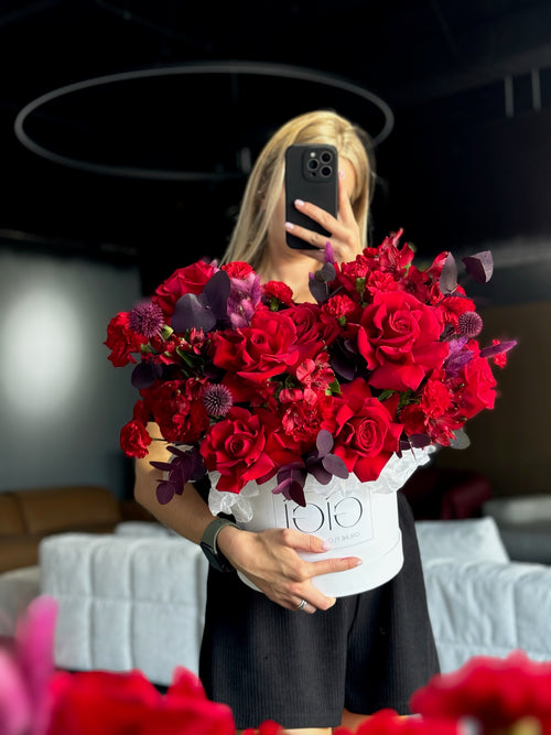 A person holding a large bouquet of red flowers, primarily roses, with a white box visible.