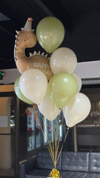 A bunch of balloons arranged to form a birthday display, with green and white balloons and a dinosaur figurine with a 'Happy Birthday' inscription.